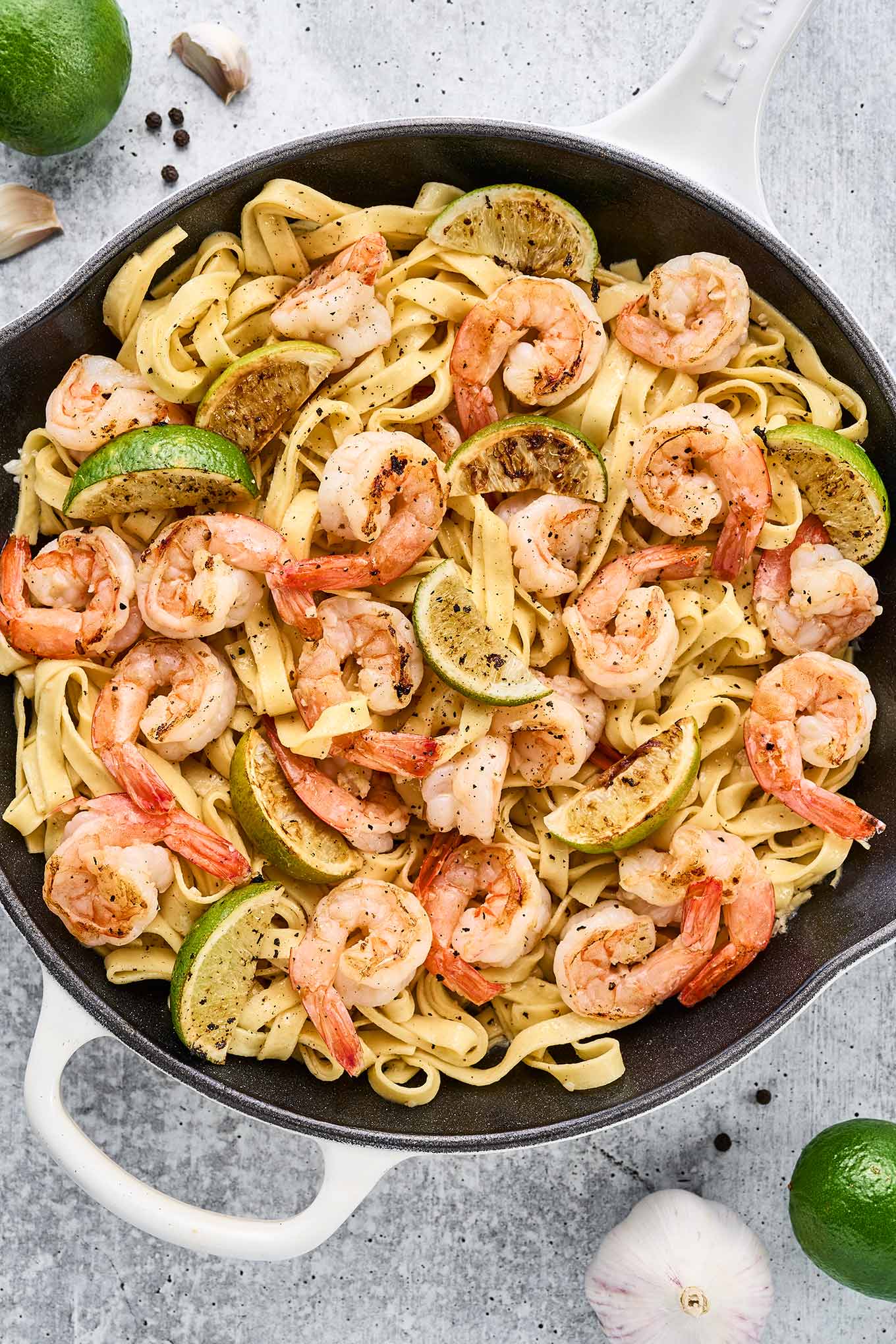 A cast iron pan filled with fettuccine tossed with sautéed shrimp, pan-seared lime wedges, and a light and garlicky white wine sauce.