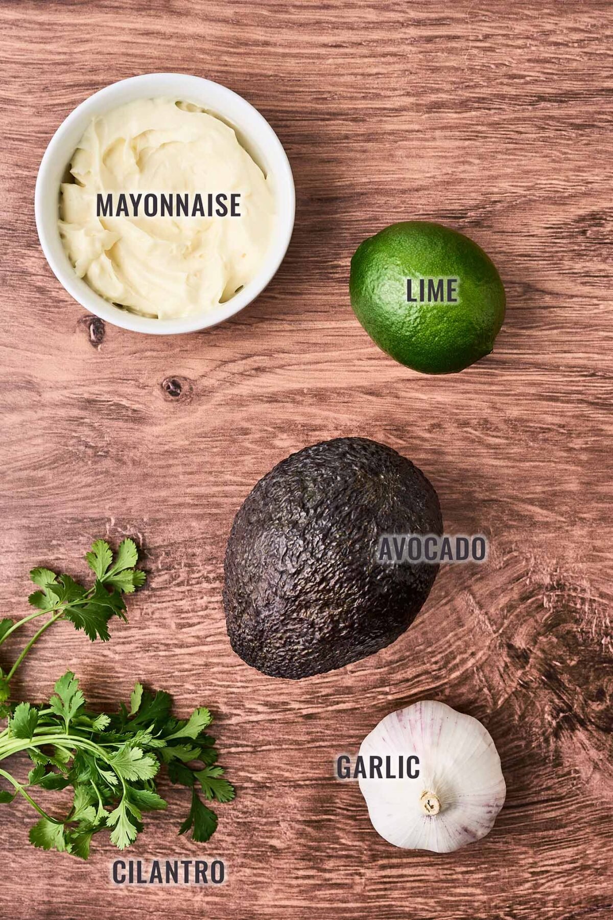 An overhead view of the ingredients needed to make avocado mayonnaise for shrimp rolls; mayonnaise, lime, Hass avocado, garlic, and cilantro.