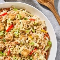 A serving bowl of Asian noodle salad with peanut dressing and crispy, golden tofu, extra peanut dressing and salad servers to the side.