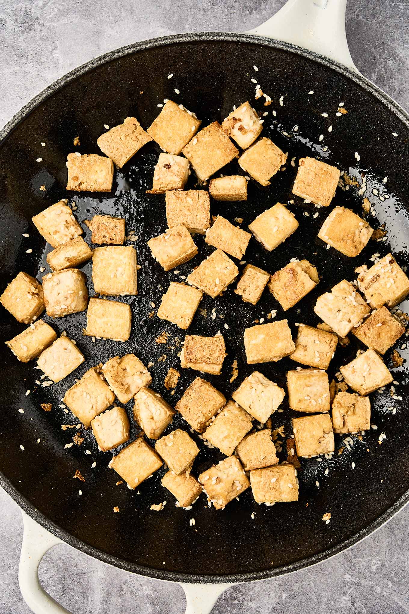 Golden brown cubes of sautéed, extra-firm tofu in a cast iron pan with sesame seeds.