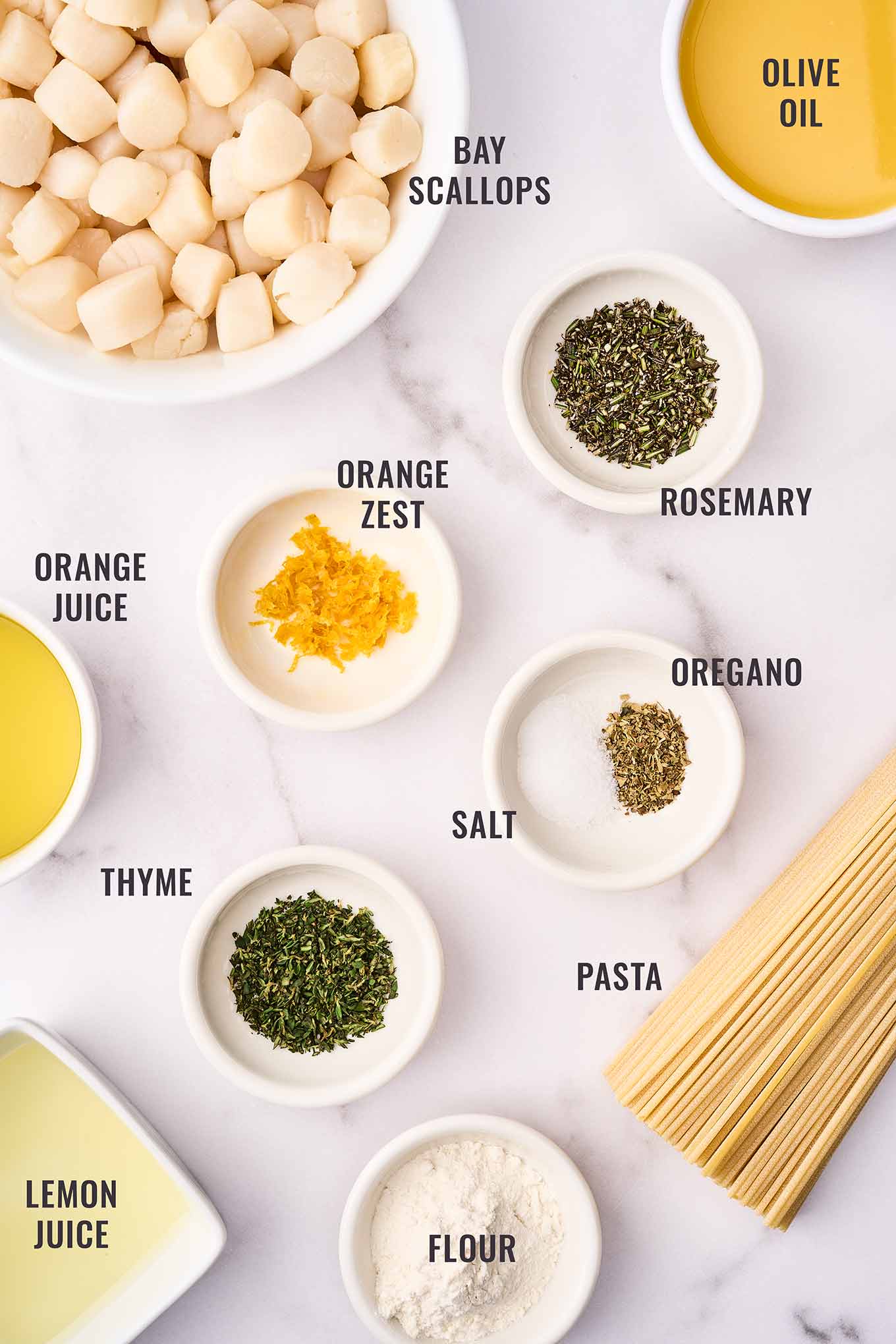 A labeled, overhead view of the ingredients needed for bay scallop pasta with citrus sauce; bay scallops, orange juice and zest, lemon juice, garlic, rosemary, oregano, thyme, olive oil, and thin spaghetti.