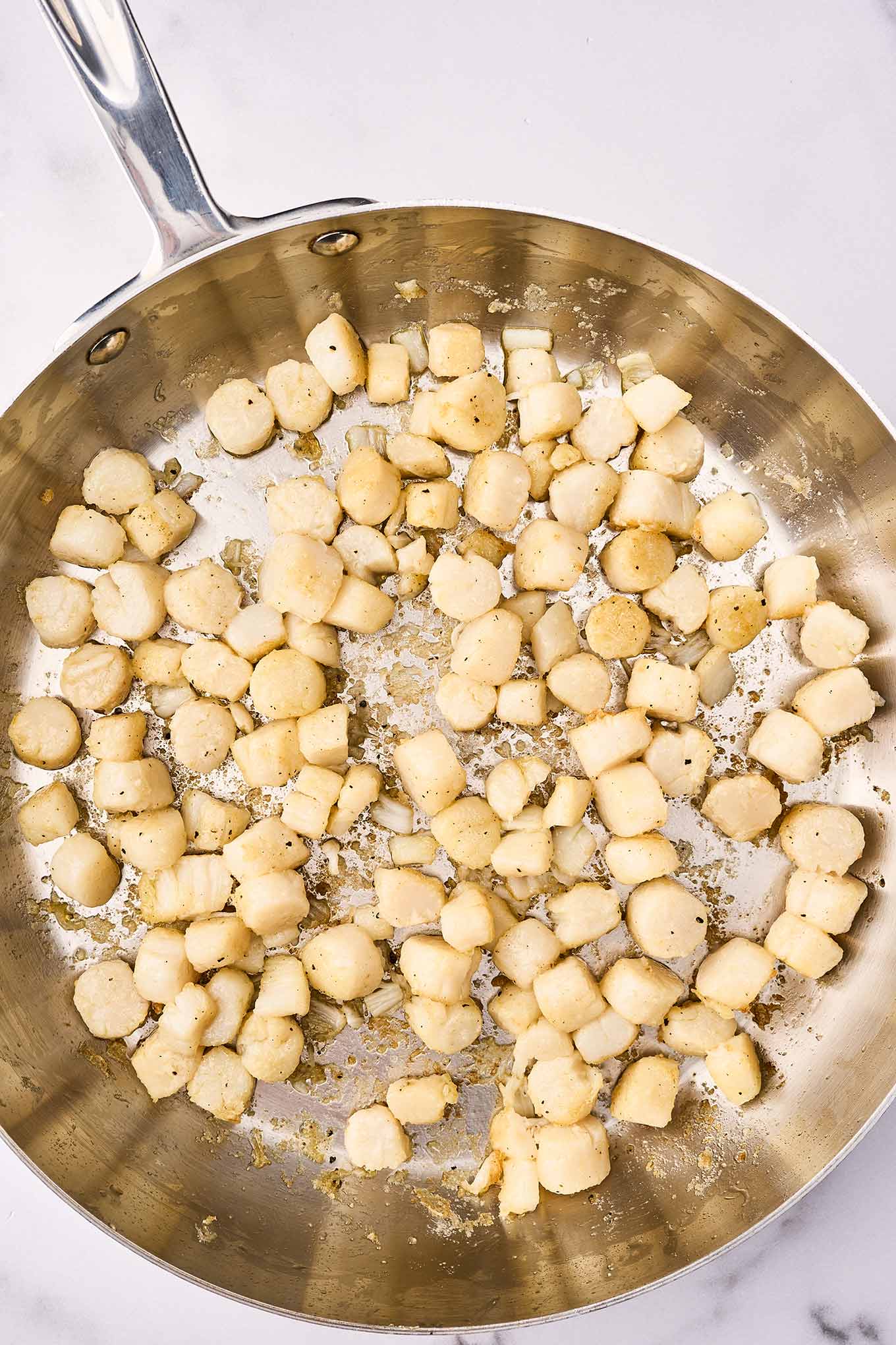 A frying pan with bay scallops being sautéed in olive oil with garlic.