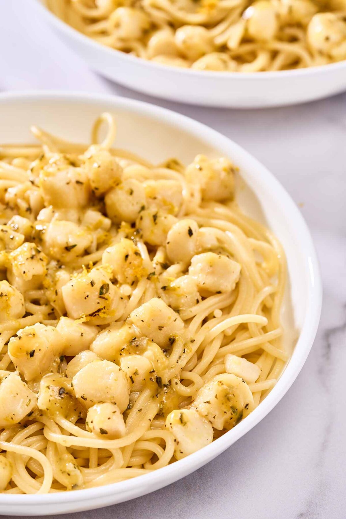 A close view of a serving of spaghetti and scallops tossed with citrus sauce showing bits of fresh herbs and orange zest.
