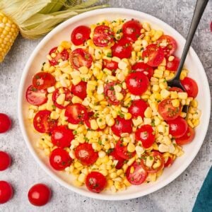 Summer recipe: A bowl of fresh corn and tomato salad with a serving spoon on a gray surface.