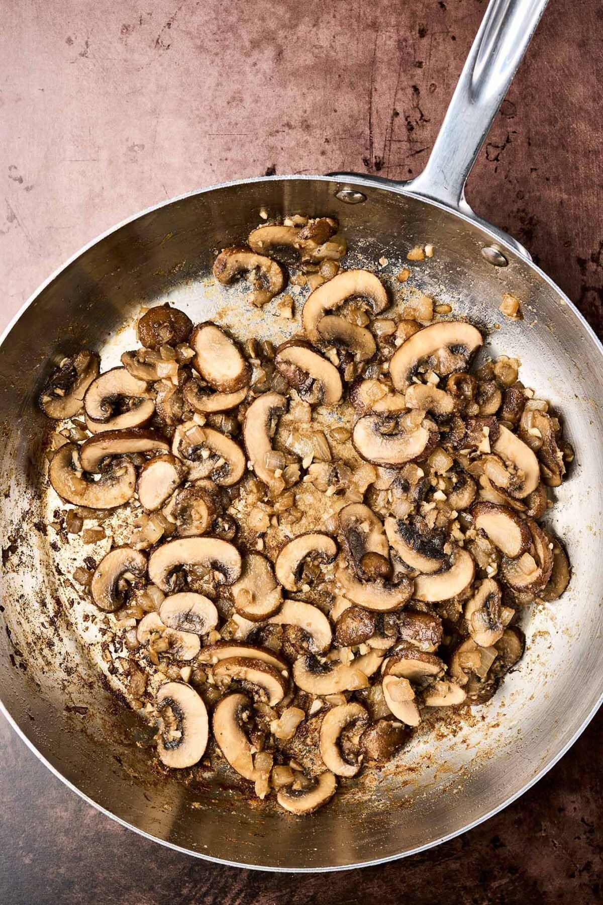 A frying pan showing beautifully browned mushrooms with garlic and onions, ready for the addition of Marsala wine to make a sauce.