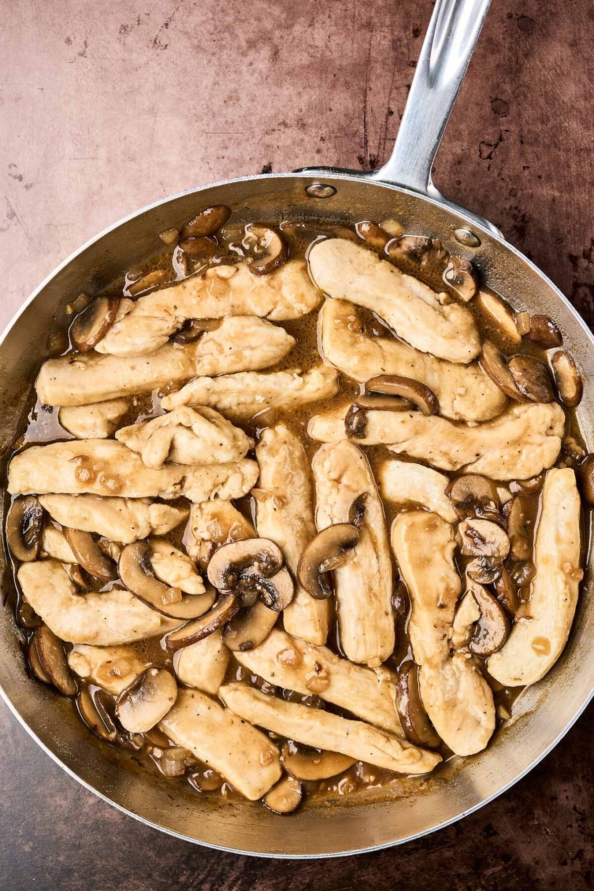 A frying pan with chicken and mushrooms sautéed with garlic and onion in Marsala wine sauce.