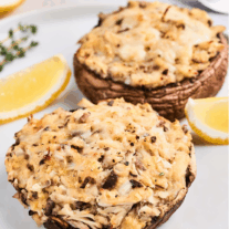 Crab-stuffed portobello mushrooms topped with melted cheese, lemon wedges and thyme sprigs as garnish, on a white plate, ready to serve.