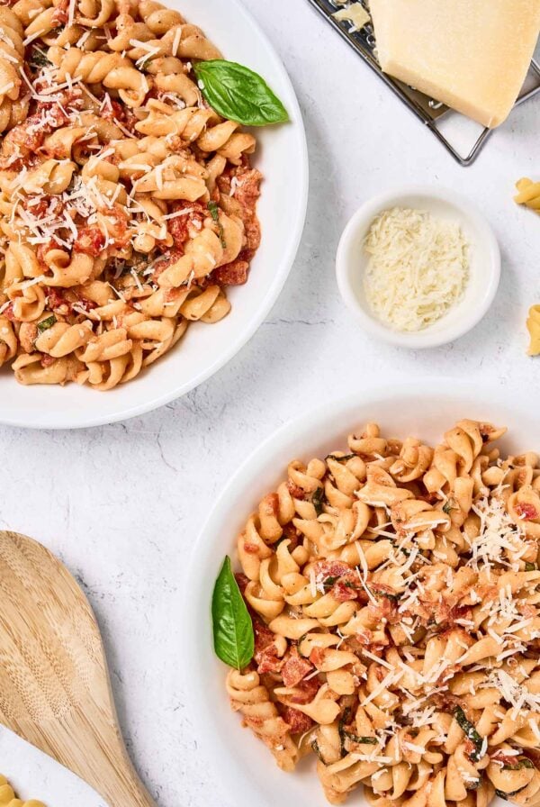 An overhead view of two bowls of fusilli pasta tossed with mascarpone tomato sauce, garnished with fresh basil, and topped with grated Parmesan cheese.