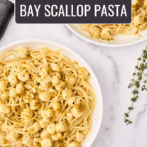 Two servings of bay scallop pasta with Sicilian citrus sauce in shallow white bowls, surrounded by a sprig of fresh thyme, and a citrus zester.