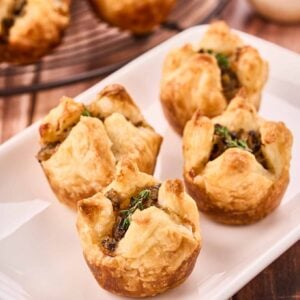 A close-up of mushroom puffs garnished with fresh thyme on an appetizer plate, more in the background.