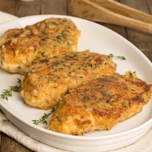 Three breaded, boneless chicken breasts on a serving platter topped with chopped thyme.