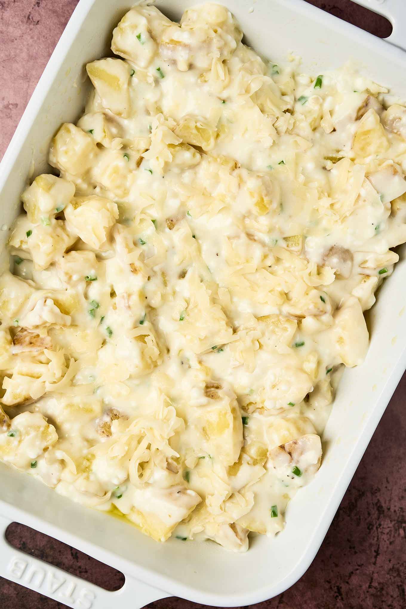 Unbaked cottage cheese potato bake in a white dish, filled with chopped potatoes with creamy cheese sauce and sprinkled with shredded Fontina, ready for the oven.