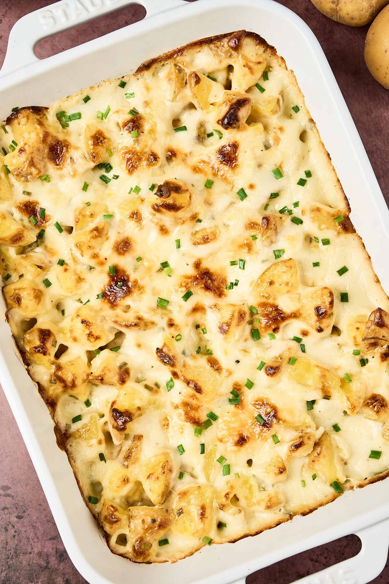 Close-up of a golden brown cottage cheese potato bake topped with melted cheese and fresh chives in a white baking dish.