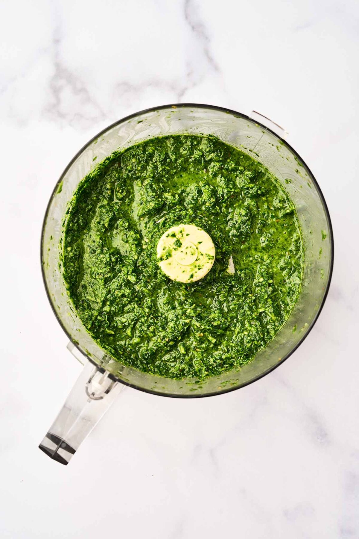 Freshly blended chimichurri sauce in a food processor, made with parsley, cilantro, garlic, and olive oil.