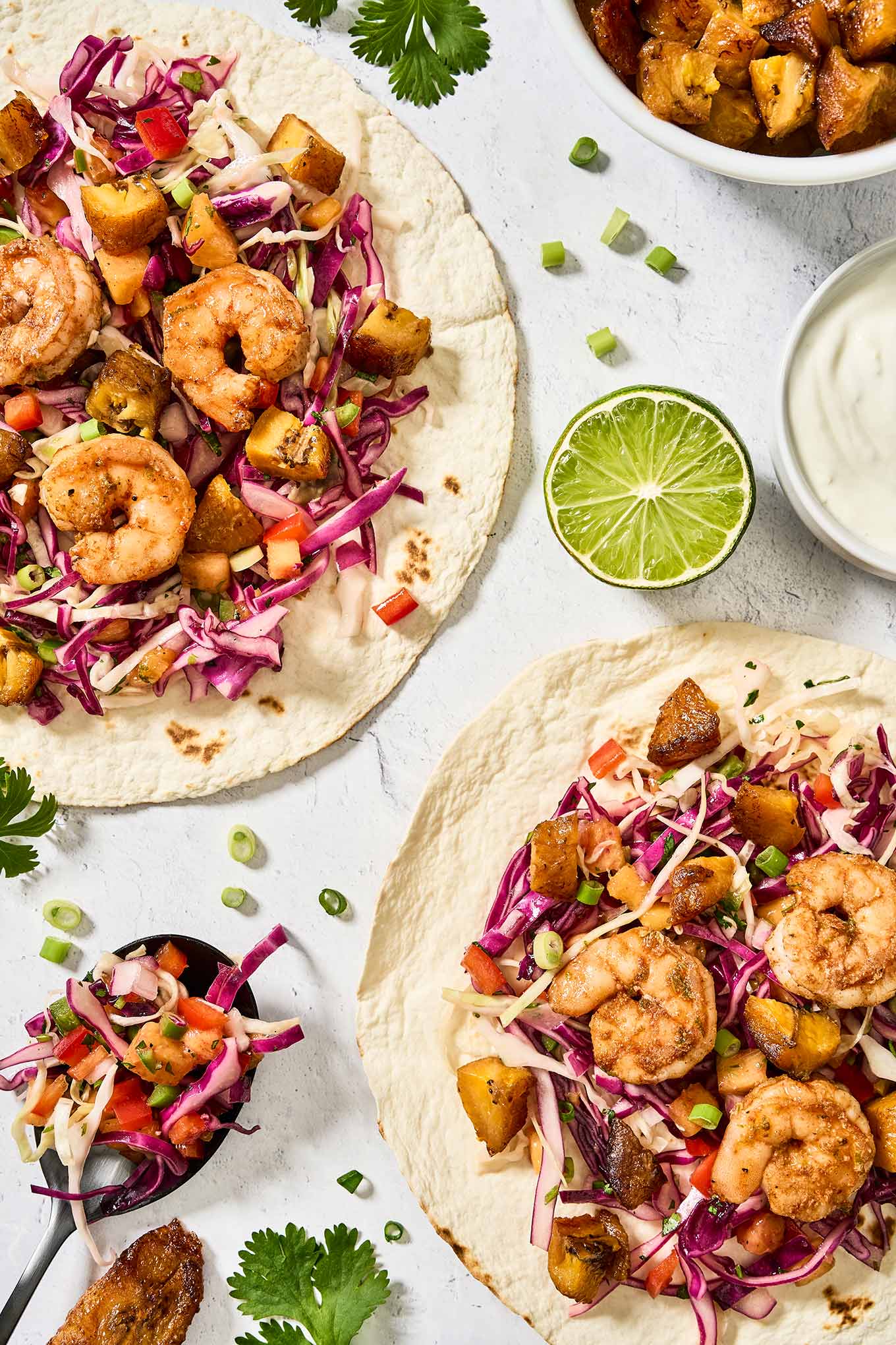 Spicy shrimp tacos with sweet plantains, tropical slaw, and lime crema on flour tortillas, garnished with cilantro and scallions.