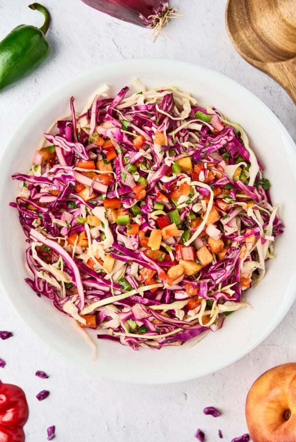 Bowl of tropical slaw with green and red cabbage, nectarine, red bell pepper, jalapeño, red onion, and cilantro tossed in a citrus dressing.