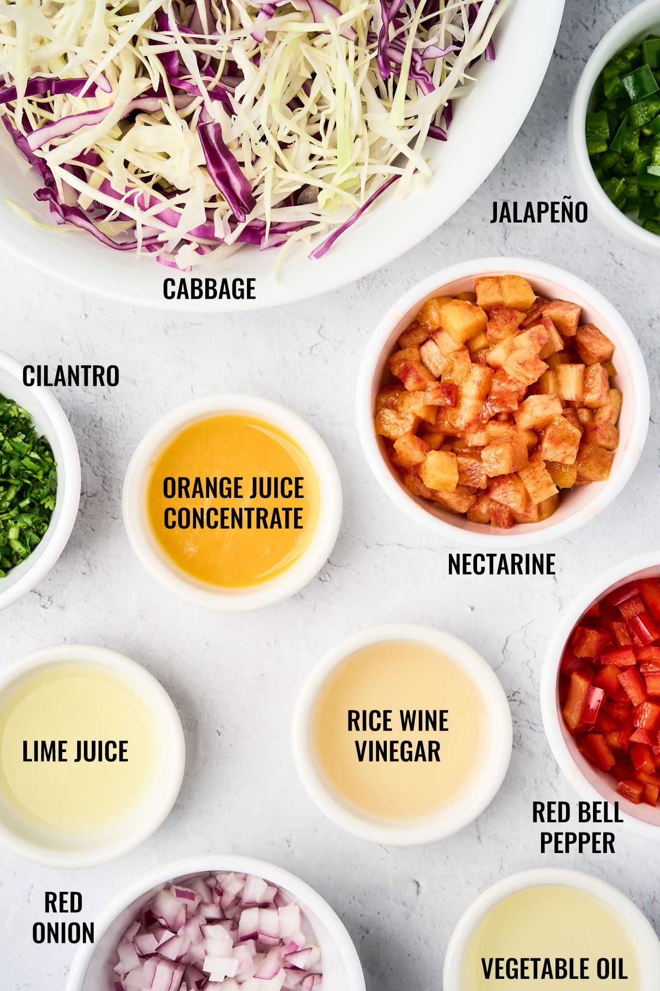 Ingredients for tropical slaw recipe including cabbage, nectarine, jalapeño, red bell pepper, red onion, cilantro, orange juice concentrate, lime juice, rice wine vinegar, and vegetable oil.