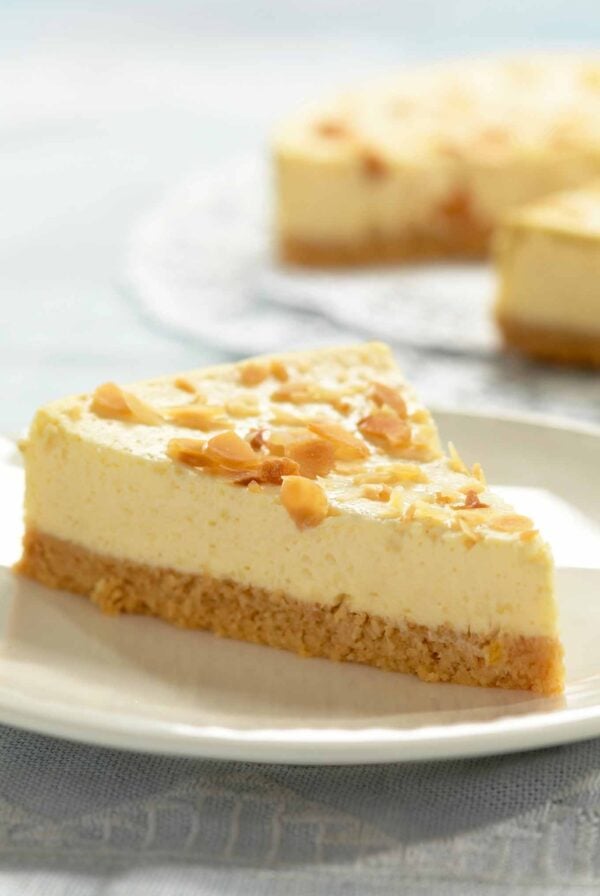A slice of amaretto cheesecake topped with sliced almonds on a plate, the remaining cheesecake in the background.
