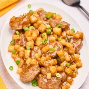 Pineapple pork medallions coated in spiced rum sauce, garnished with chopped green onions on a white plate.