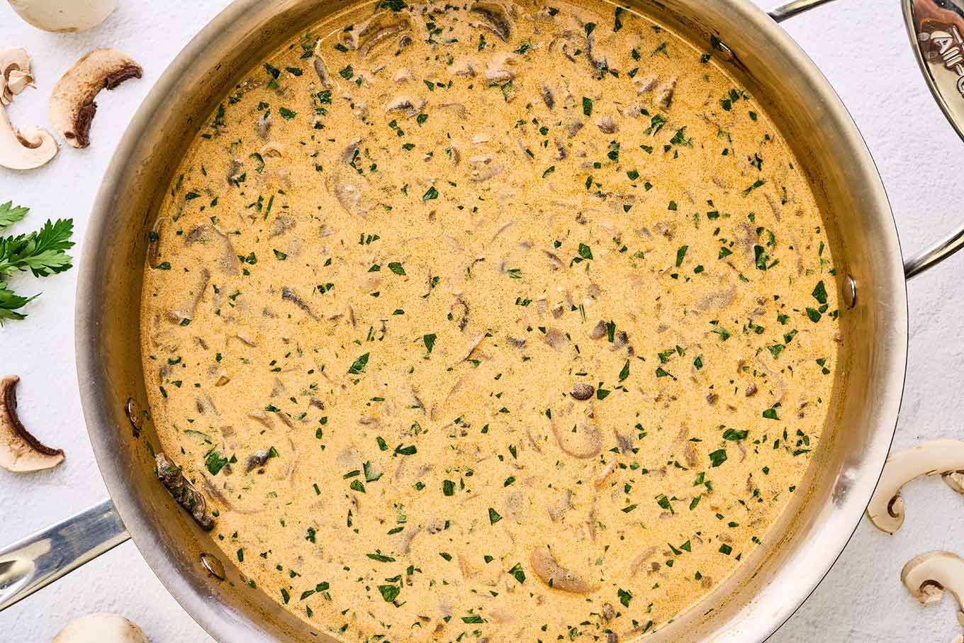 Finished Hungarian mushroom soup in a stainless steel skillet, seasoned with paprika, thickened with egg yolks and sour cream, and garnished with fresh parsley.