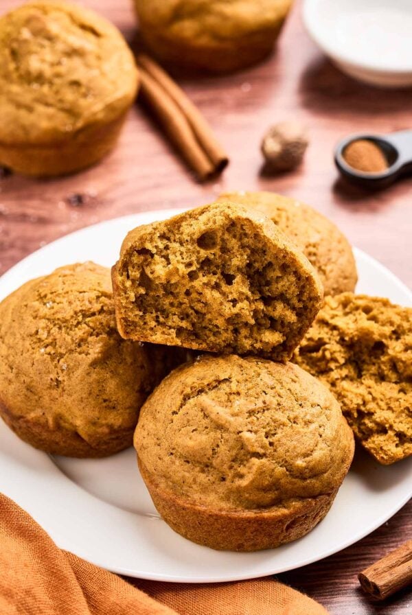 Close-up of moist and fluffy pumpkin spice muffins on a plate, one cut open to show soft texture, cinnamon sticks in the background.