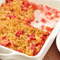 A white casserole of rhubarb pineapple crisp, one portion removed.