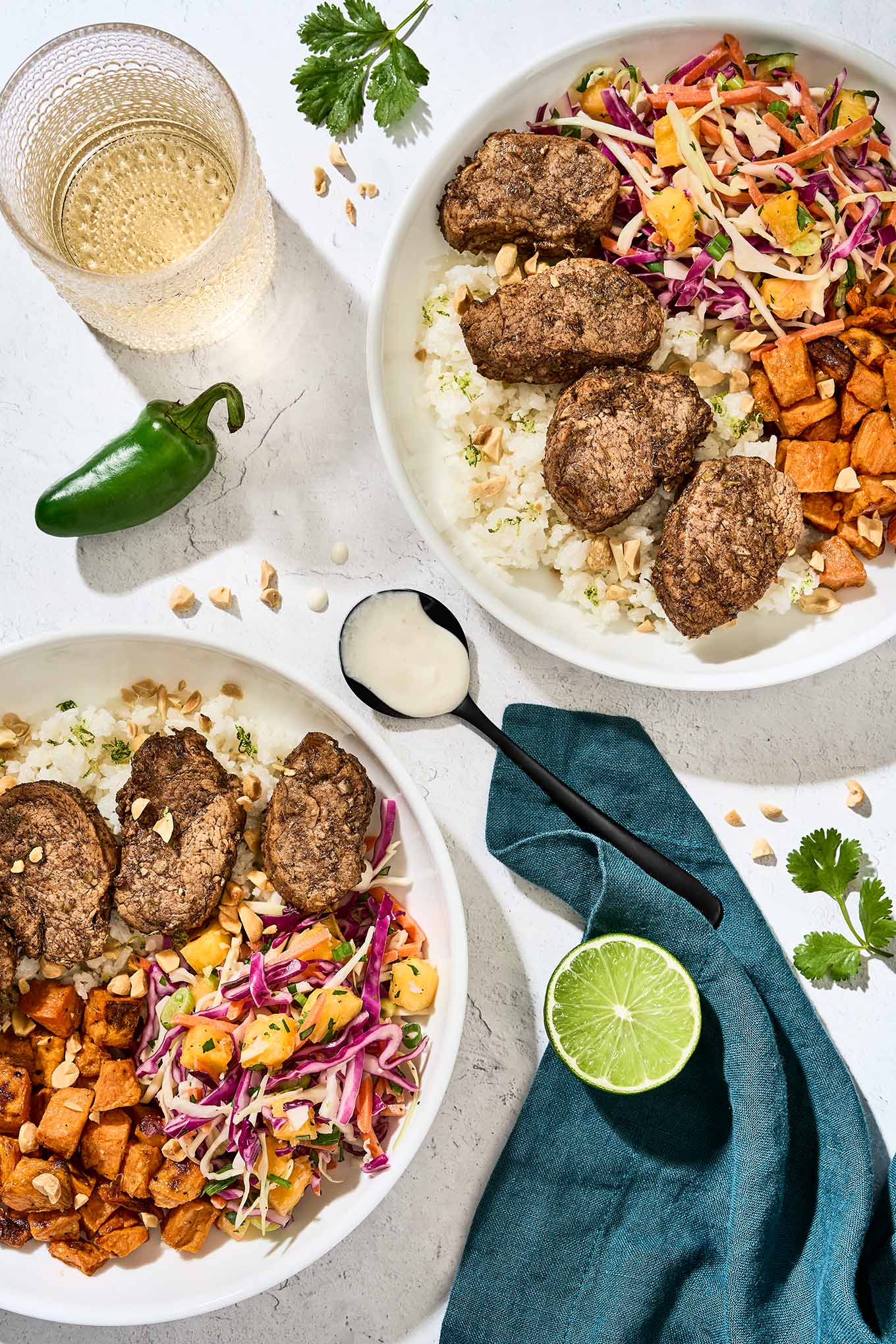 Jerk pork tenderloin slices served over coconut lime rice, with pineapple slaw, and roasted sweet potatoes, garlic-lime drizzle on a spoon in the center.