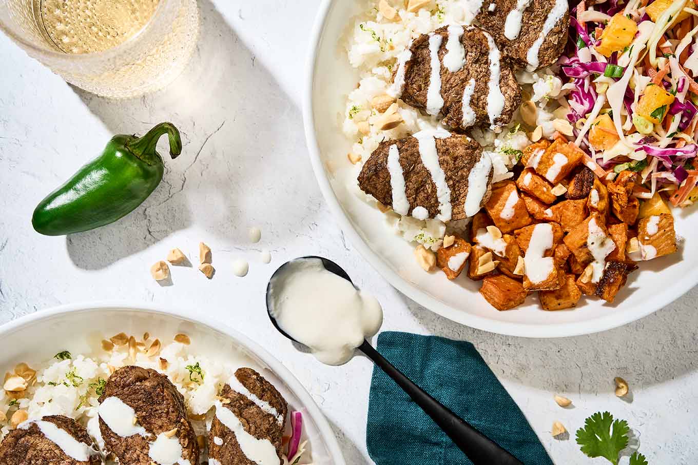 Jerk pork tenderloin with garlic-lime drizzle served in a bowl over coconut lime rice, cubed roasted sweet potatoes, and pineapple slaw.