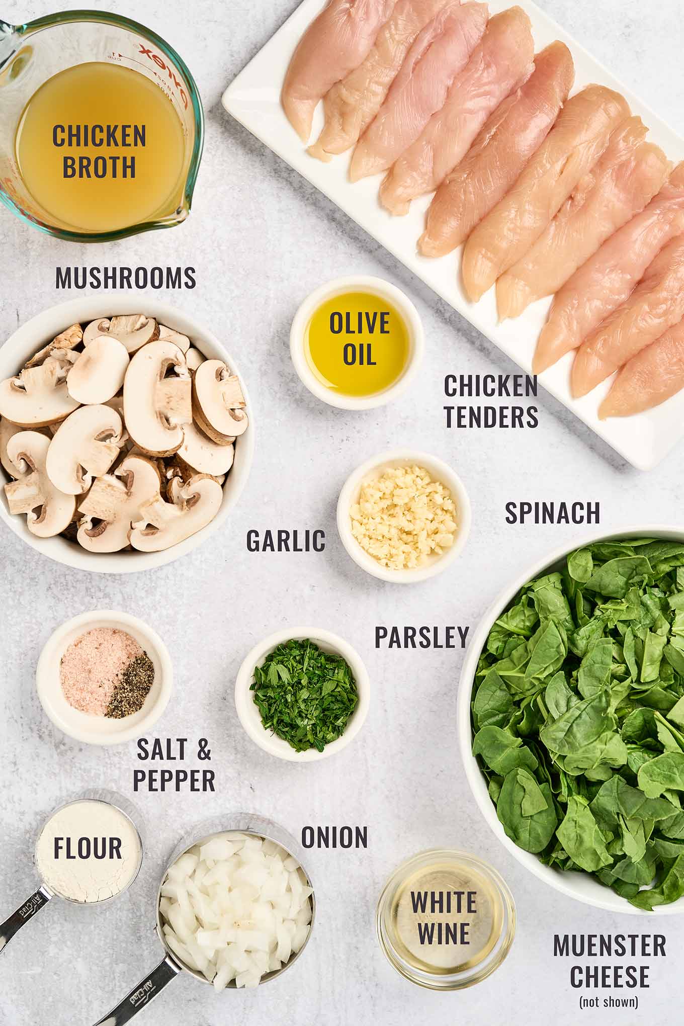 An overhead view of the ingredients for making mushroom chicken with spinach; chicken tenderloins, sliced mushrooms, fresh spinach, onion, garlic, white wine and more.