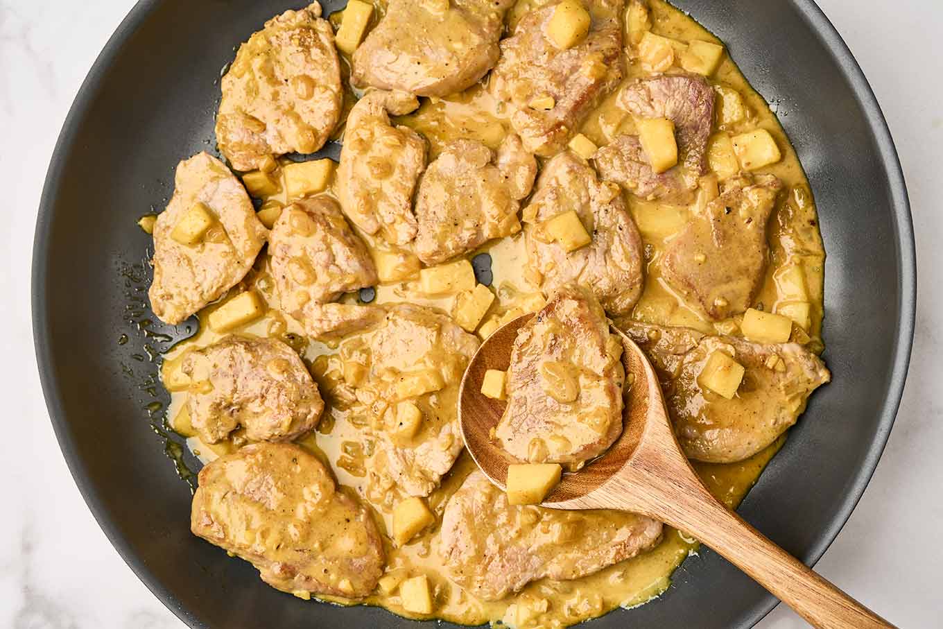The final step in preparing pork curry with apples, adding the pork medallions back to the pan to finish cooking along with the apples in the creamy curry sauce.