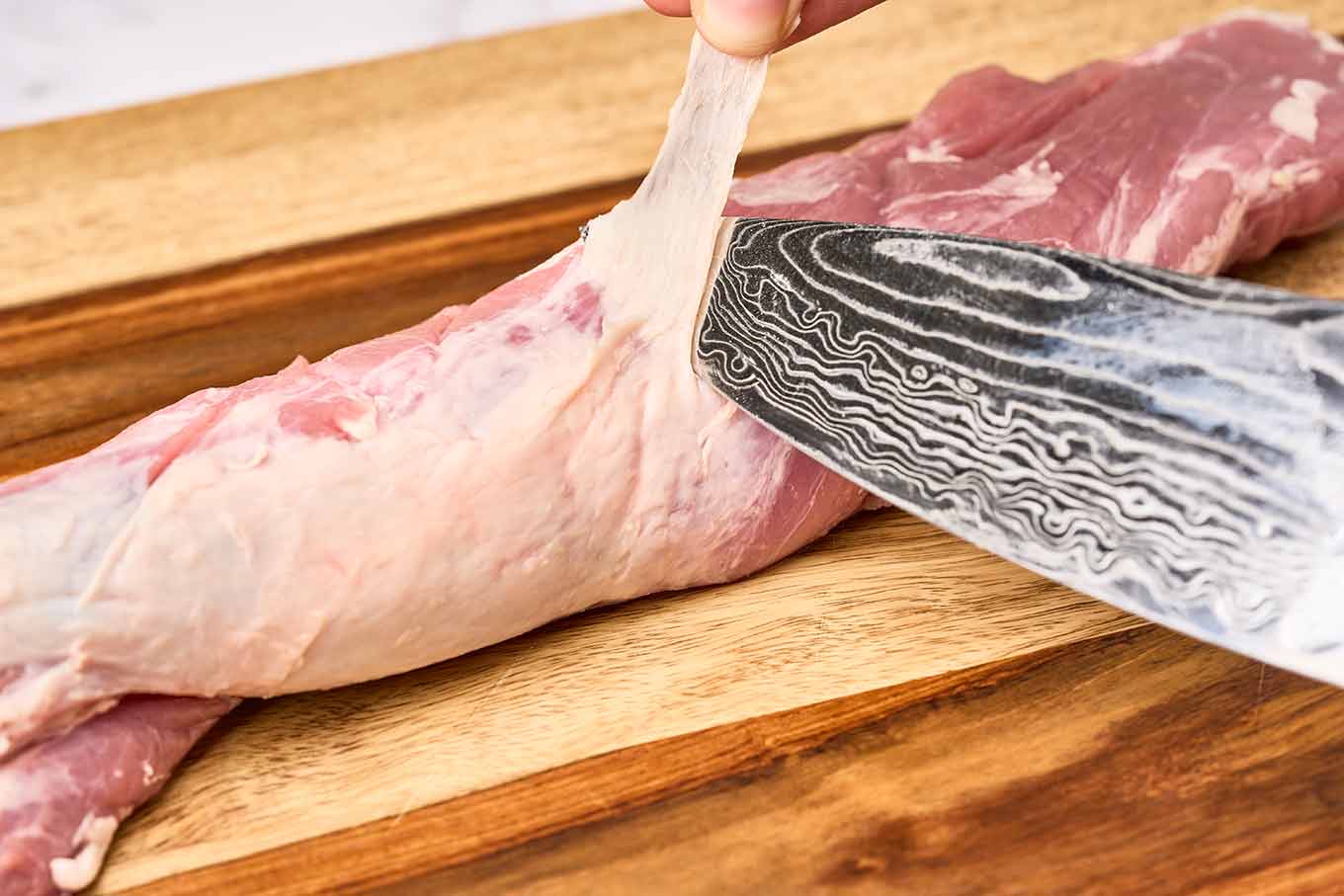 A close-up photo showing how to trim the silverskin from a pork tenderloin.