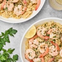 Shrimp scampi with orzo pasta served in white bowls, garnished with parsley and lemon wedges.