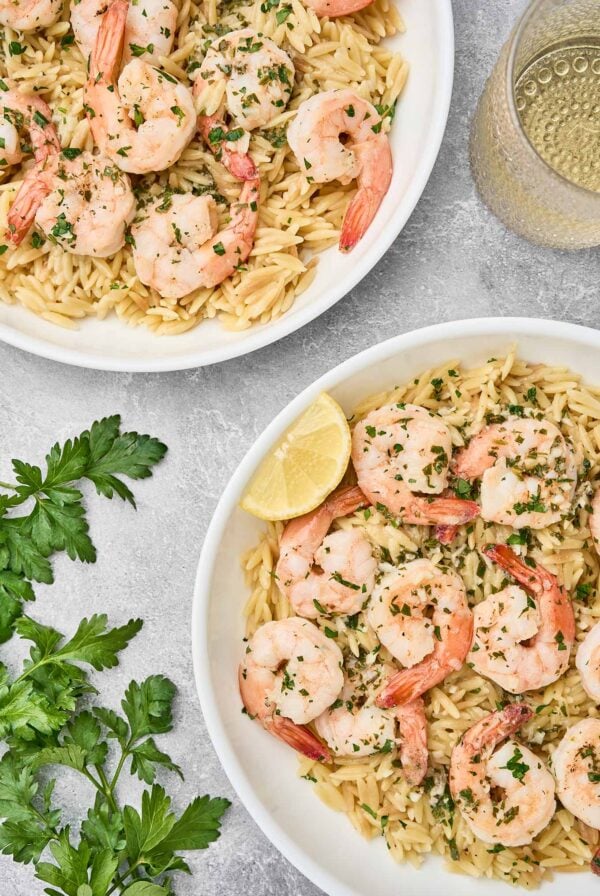 Shrimp scampi with orzo pasta served in white bowls, garnished with parsley and lemon wedges.