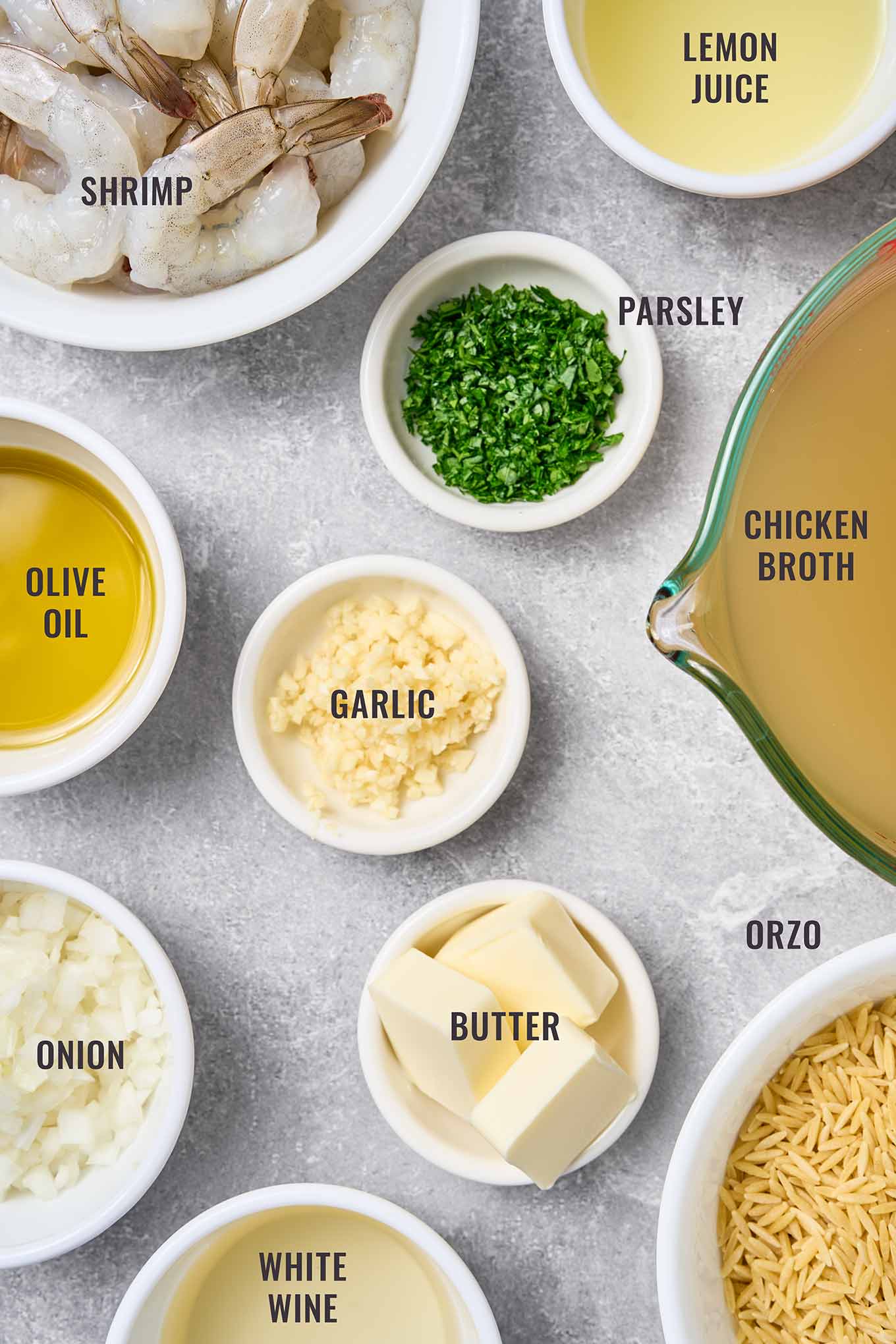A labeled, overhead photo of the ingredients for making shrimp scampi with orzo; jumbo shrimp, orzo, garlic, butter, olive oil, onion, white with, chicken broth, lemon juice, and parsley.