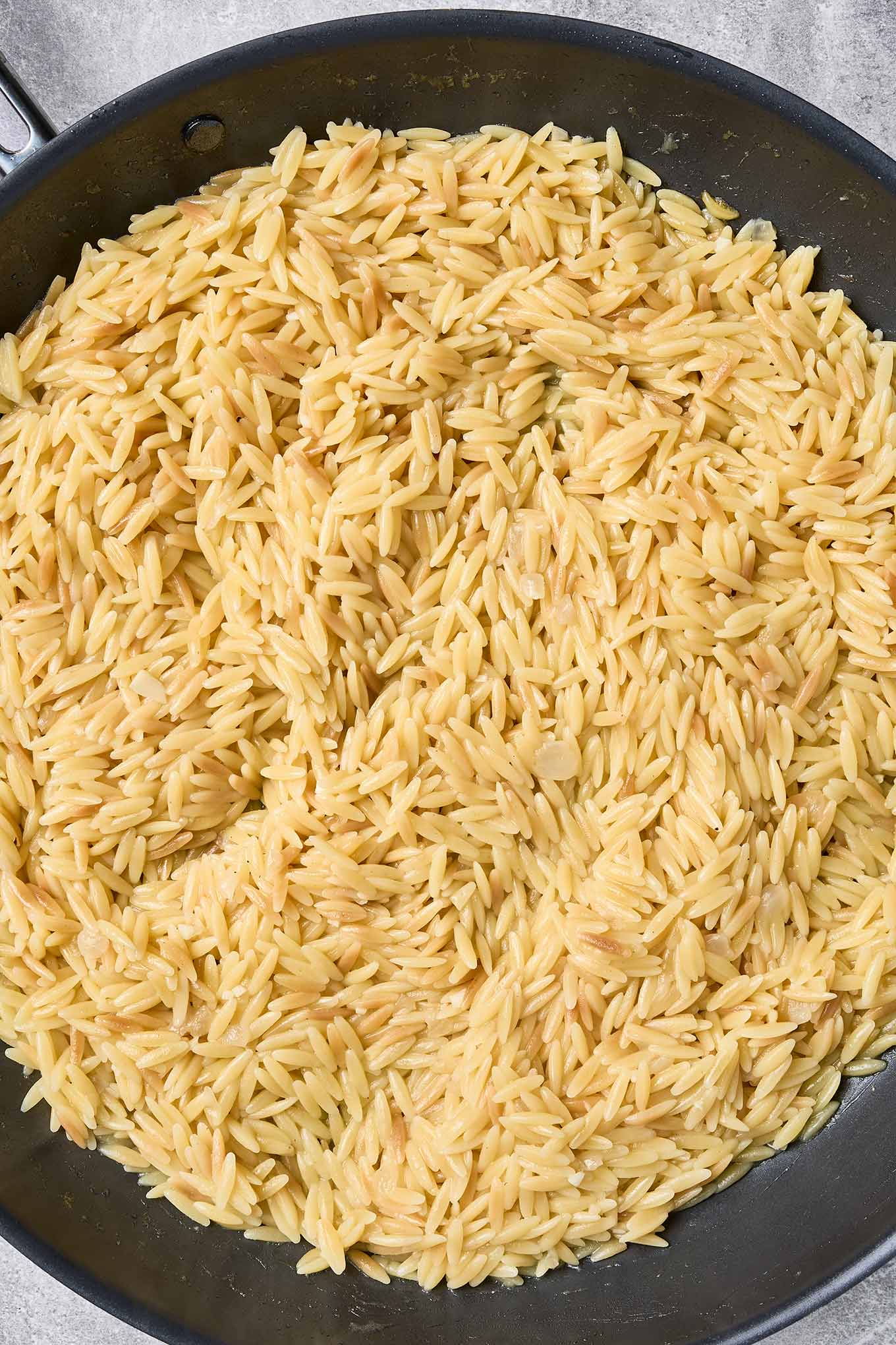 Cooked orzo in a skillet, tender and fluffy after simmering in chicken broth for shrimp scampi with orzo.