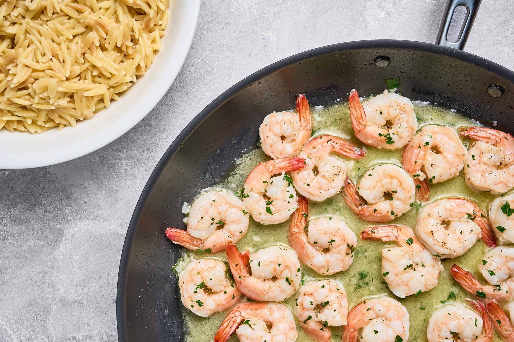 Shrimp scampi simmering in garlic butter sauce, next to a bowl of cooked orzo ready for plating.