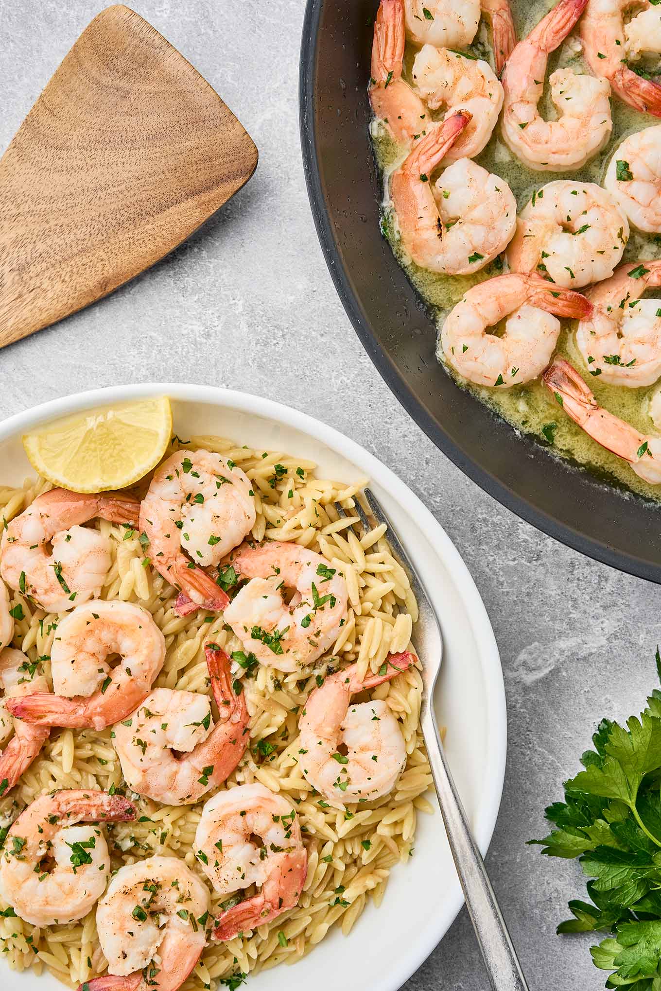 Garlic butter shrimp scampi cooking in a pan with a plated bowl of shrimp and orzo pasta garnished with herbs and a lemon wedge.