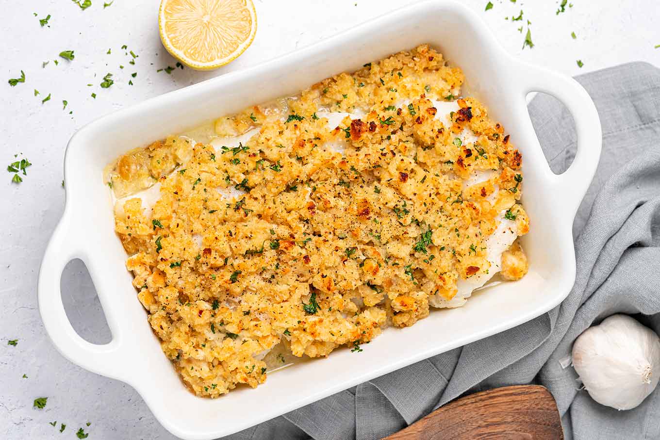 The first of two oven-baked seafood dishes to serve as a main course for a Feast of the Seven Fishes; baked cod with a garlic butter crumb topping in an white baking dish with handles.
