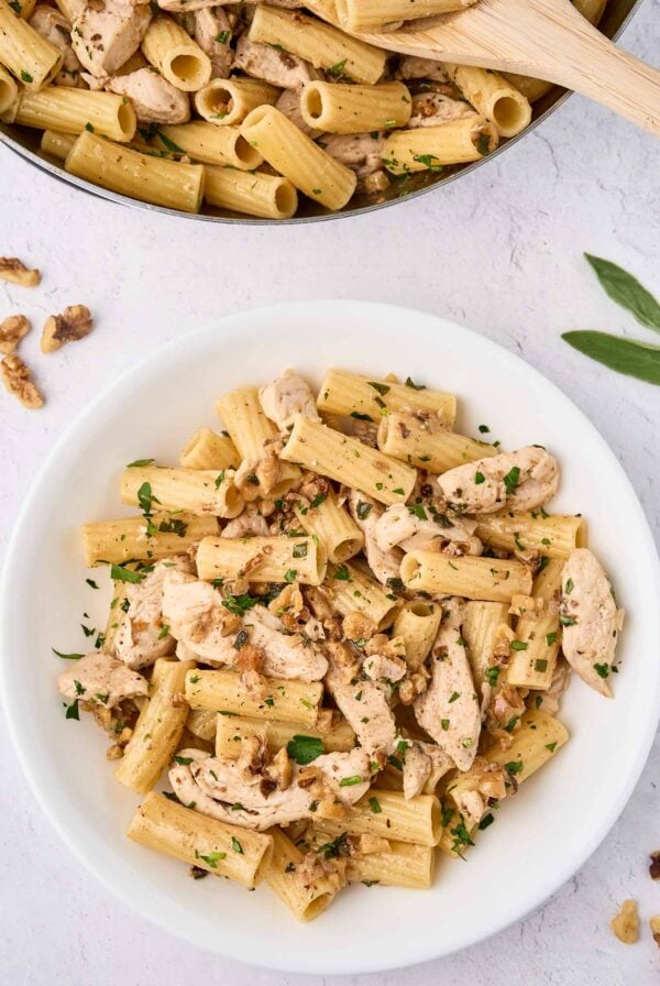 An overhead view of brown butter chicken pasta being spooned into a serving bowl from the skillet.