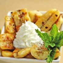Bowl of Caribbean bananas caramelized in butter, brown sugar, rum, and lime, topped with whipped cream and garnished with fresh mint.