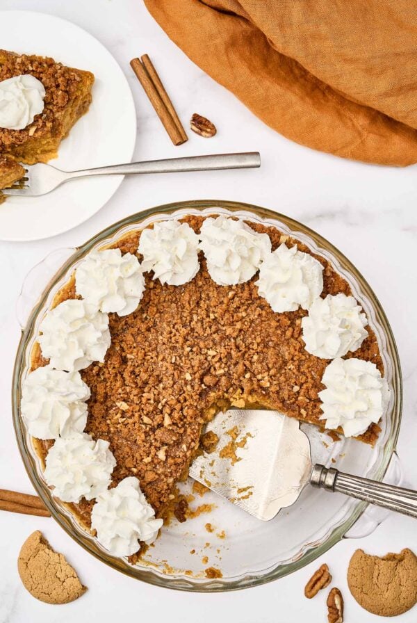 Crustless pumpkin pie with pecan gingersnap streusel and whipped cream, one slice served on a plate.
