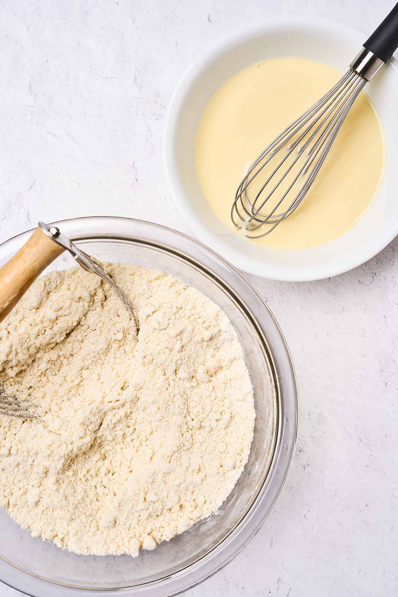 Making Golden Delicious apple cake; two mixing bowls, one with dry ingredients showing consistency, another bowl with wet ingredients and a whisk.