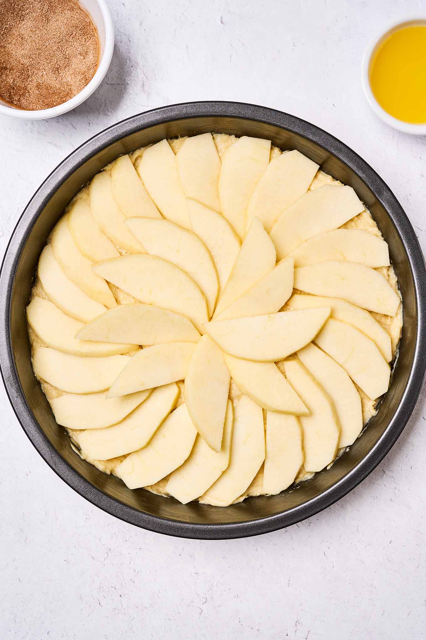 Golden Delicious apple cake batter in the pan and topped with apple slices, waiting to be topped with melted butter and cinnamon sugar.