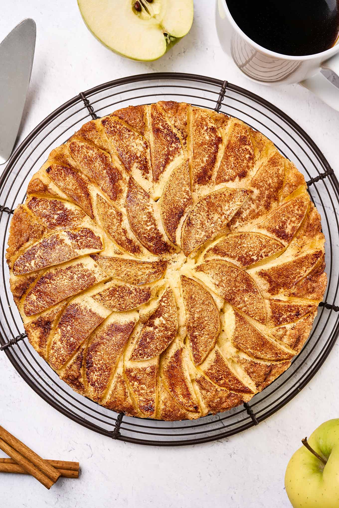 Freshly baked apple cake topped with sliced Golden Delicious apples and cinnamon sugar, cooling on a wire rack, waiting to be sliced.
