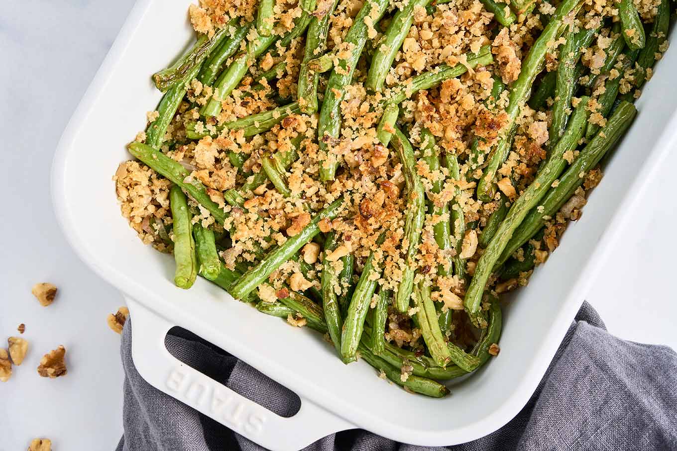 Roasted green beans in a white casserole dish, finished with a crisp buttery topping of walnuts and panko crumbs.