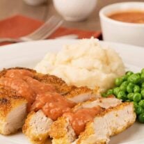 Pan-fried chicken with Southern tomato gravy served with mashed potatoes and green peas on a white plate.