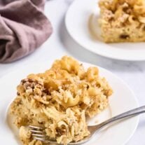 Slice of sweet noodle kugel on a white plate with a fork, showing its crisp cinnamon topping and tender egg noodles.