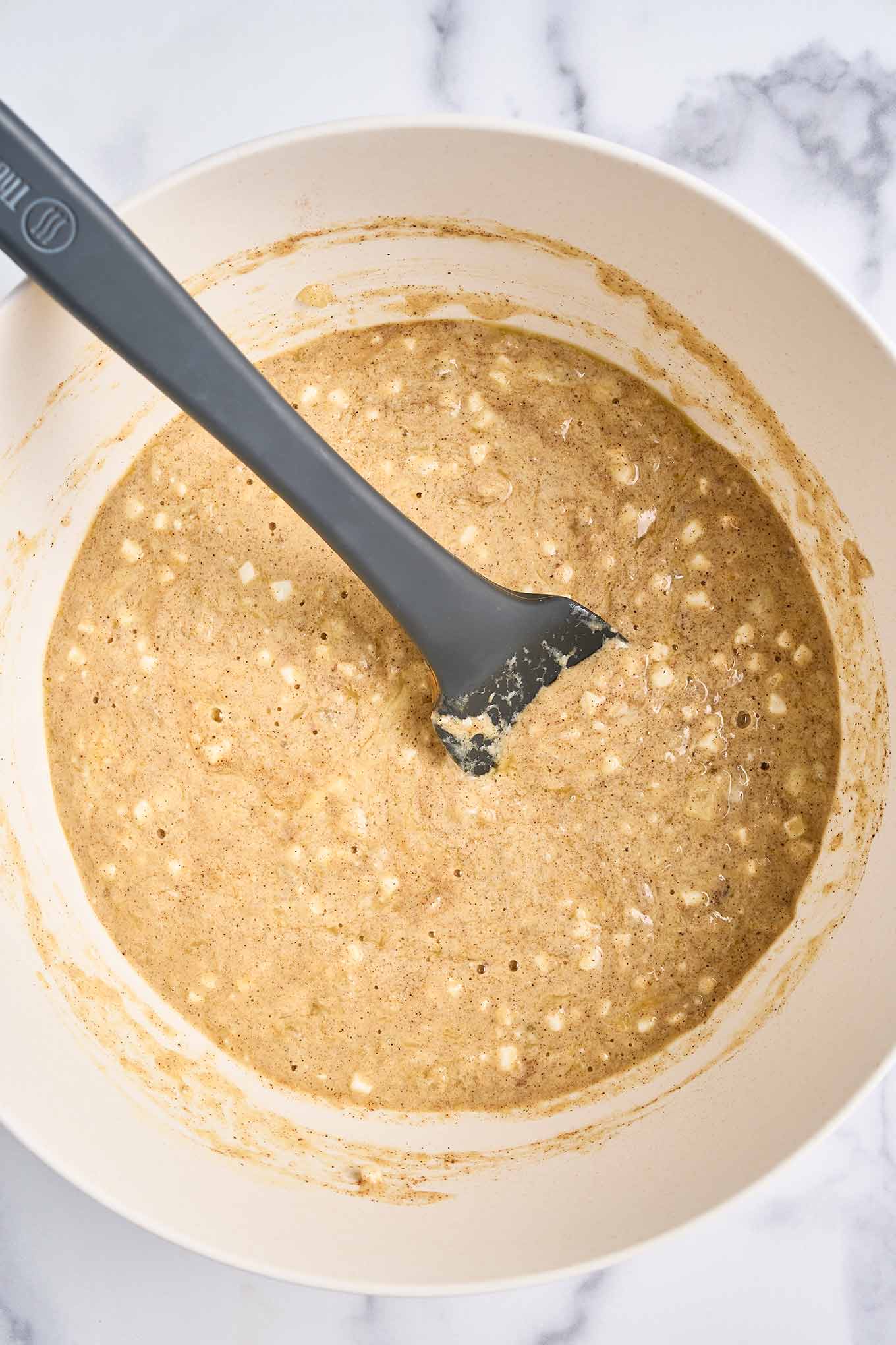 Cinnamon-speckled custard mixture with cottage cheese stirred in a mixing bowl with a spatula.
