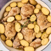 Braised chicken legs with baby potatoes, garlic, and thyme in a large pan after cooking.