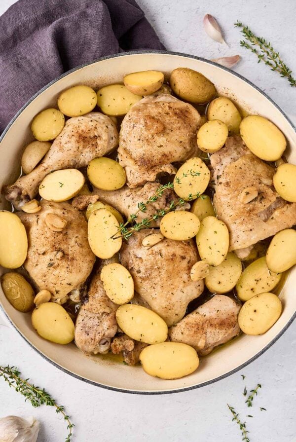 Braised chicken legs with baby potatoes, garlic, and thyme in a large pan after cooking.